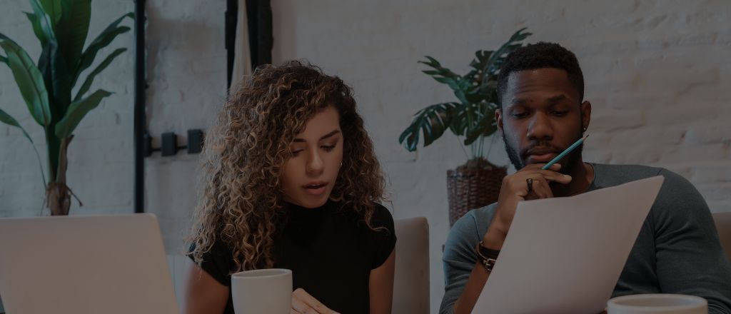 A man and a woman reviewing renovation paperwork at a desk, with a laptop and coffee cup, planning the budget and timeline for a bathroom renovation.