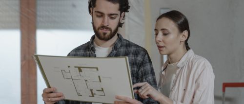 A man and a woman discussing a bathroom renovation plan with design sketches on the table.