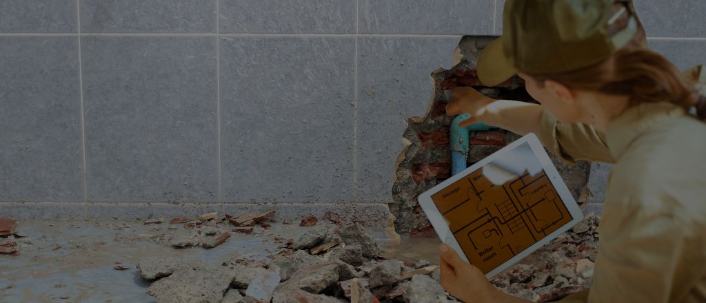 A plumber inspecting a damaged pipe hidden behind bathroom tiles during a renovation.