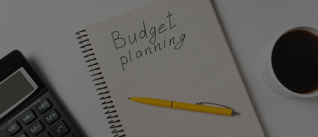 Top view of a desk with a calculator, a notebook labeled 'Budget Planning', a yellow pen, and a cup of coffee.