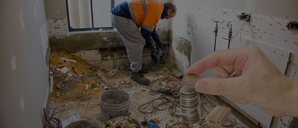 Worker using a drill to remove bathroom tiles, overlaid with a transparent image of a hand holding coins representing bathroom renovation costs in Australia 2025.